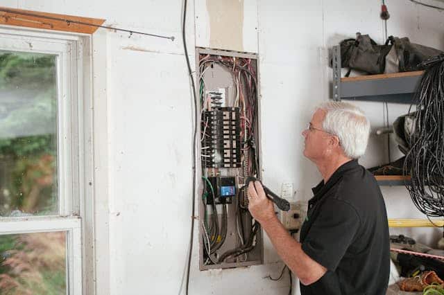 Man inspecting electrical fuse box in a garage.