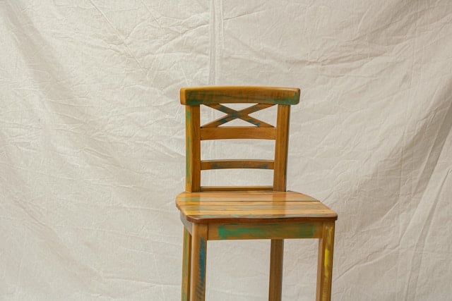 A chair that has been lightly painted to be upcycled in front of a white sheet.