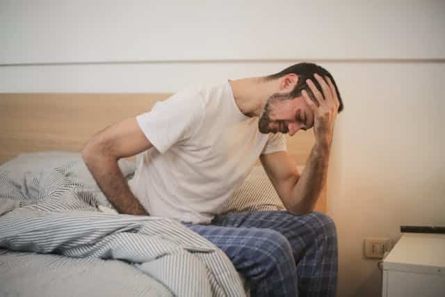 A man in bed clutching is head in one hand due to a headache