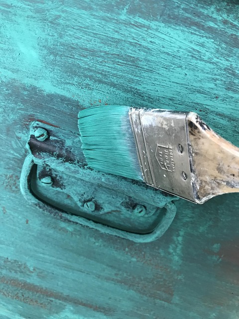 A paint brush covering a dresser in teal blue paint with large stroke marks